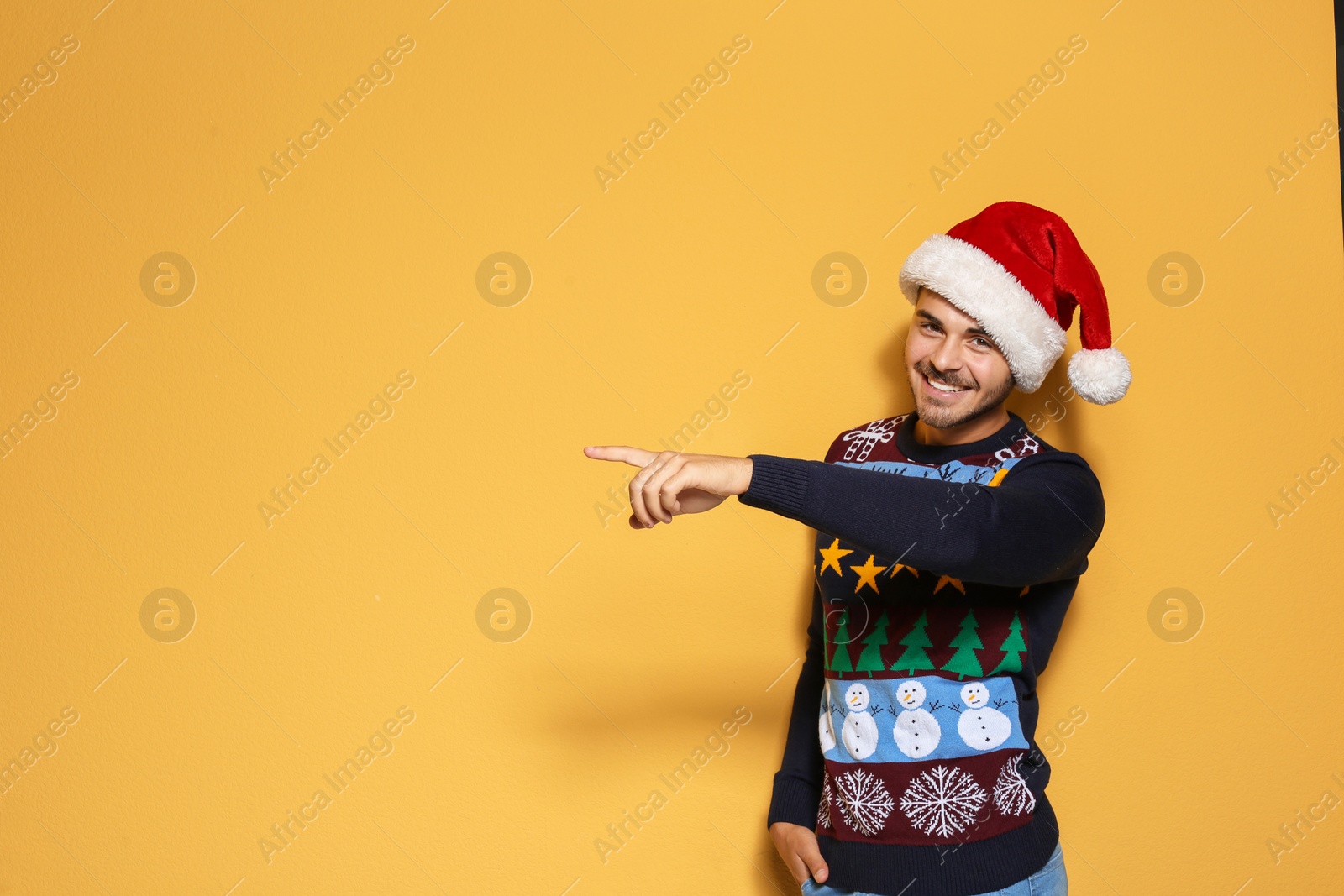 Photo of Young man in Christmas sweater and hat on color background. Space for text