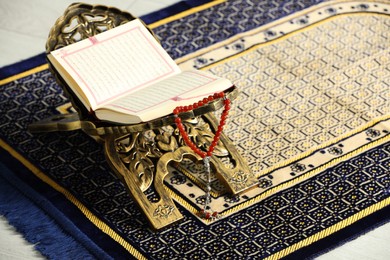 Photo of Rehal with open Quran and Misbaha on Muslim prayer rug, space for text
