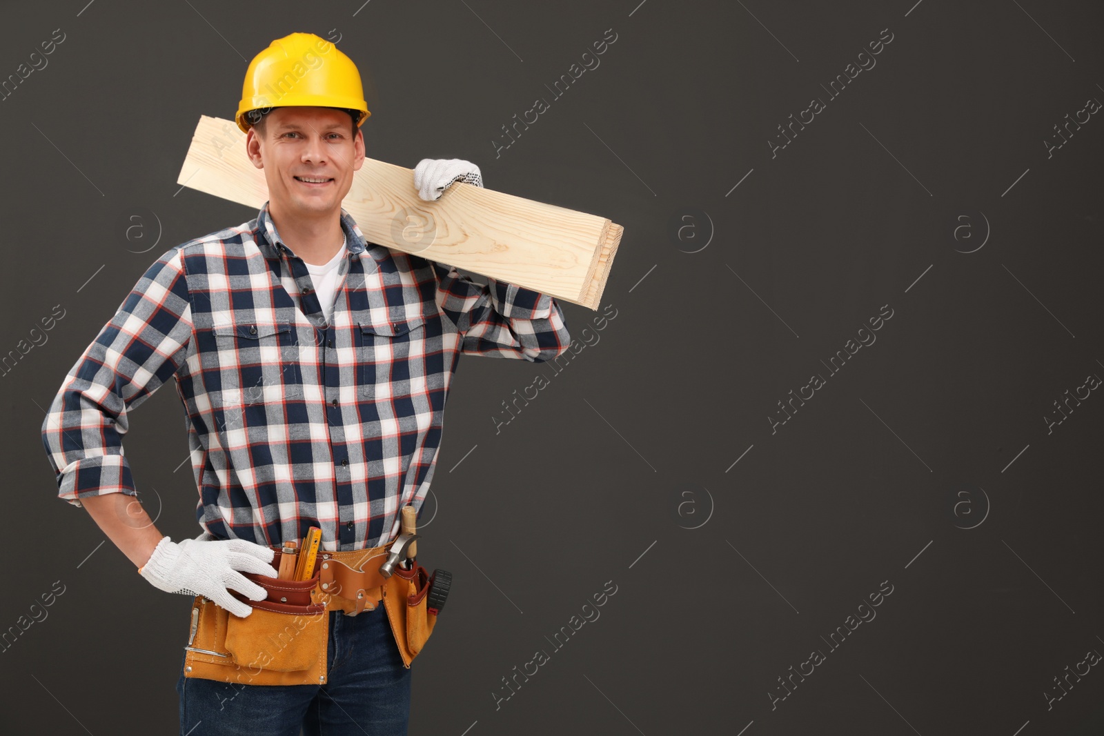 Photo of Handsome carpenter with wooden planks on dark background. Space for text