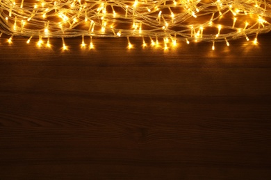 Photo of Beautiful glowing Christmas lights on wooden table, top view. Space for text