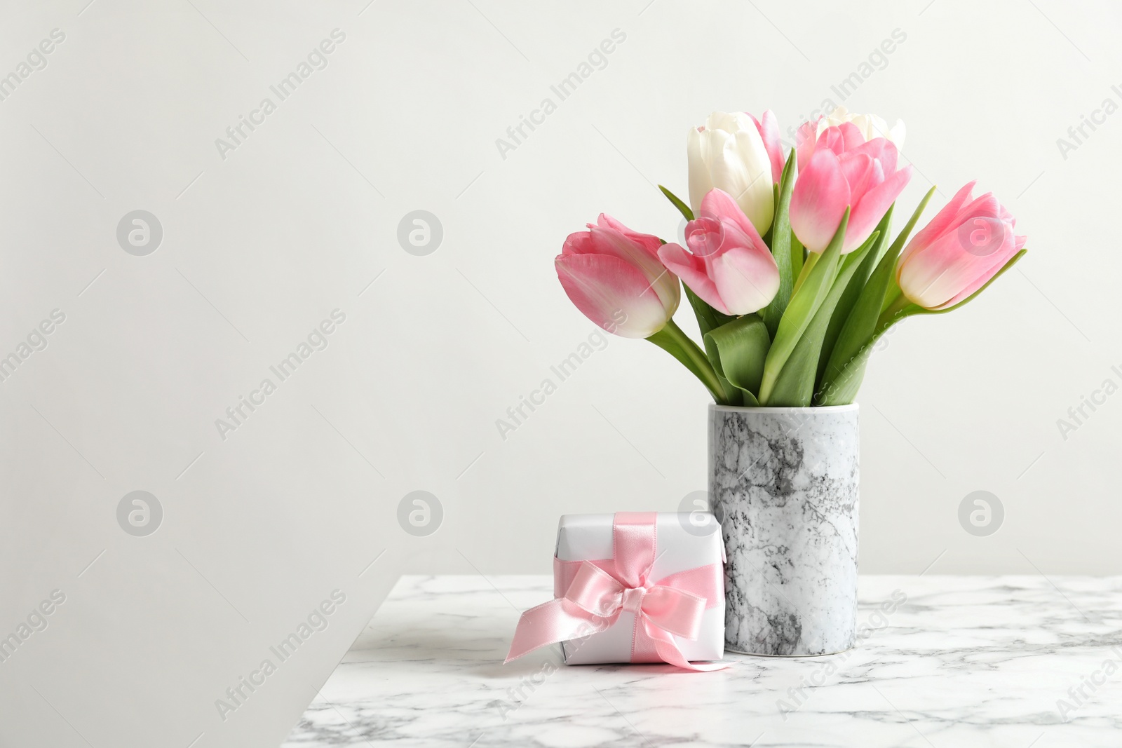 Photo of Bouquet of beautiful spring tulips in vase and gift box on marble table against light background. International Women's Day