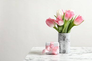 Bouquet of beautiful spring tulips in vase and gift box on marble table against light background. International Women's Day