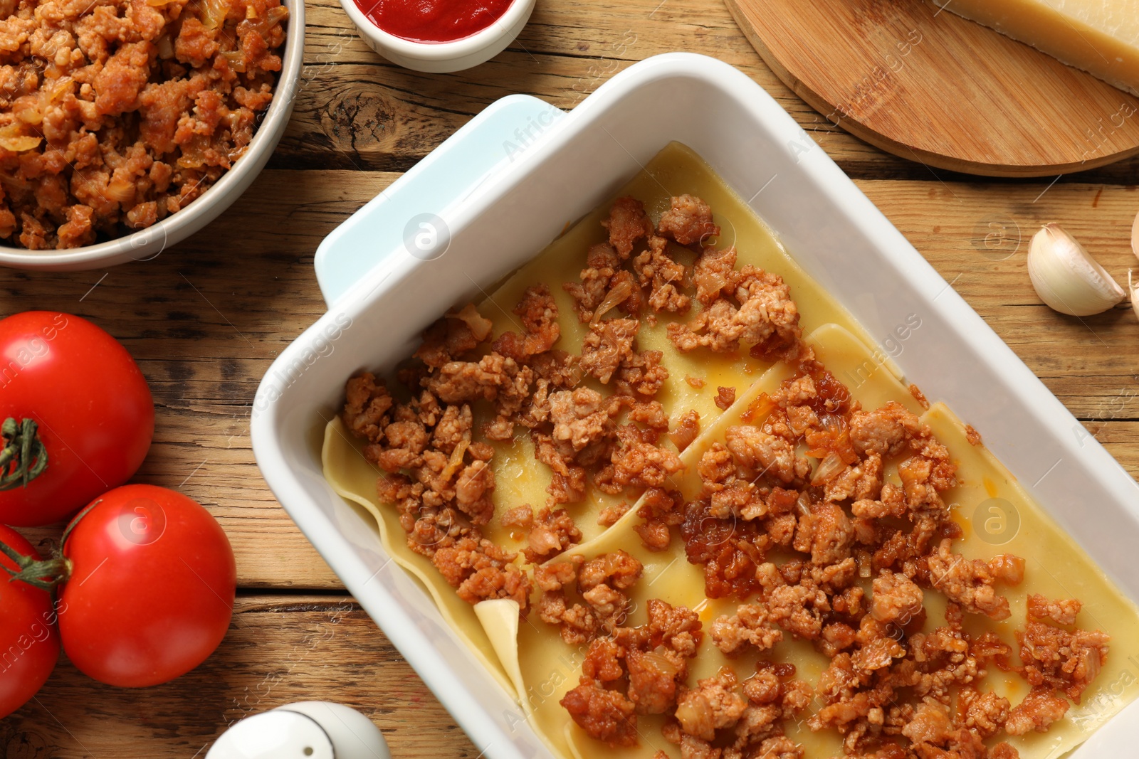 Photo of Cooking lasagna. Pasta sheets and minced meat in baking tray on wooden table, flat lay