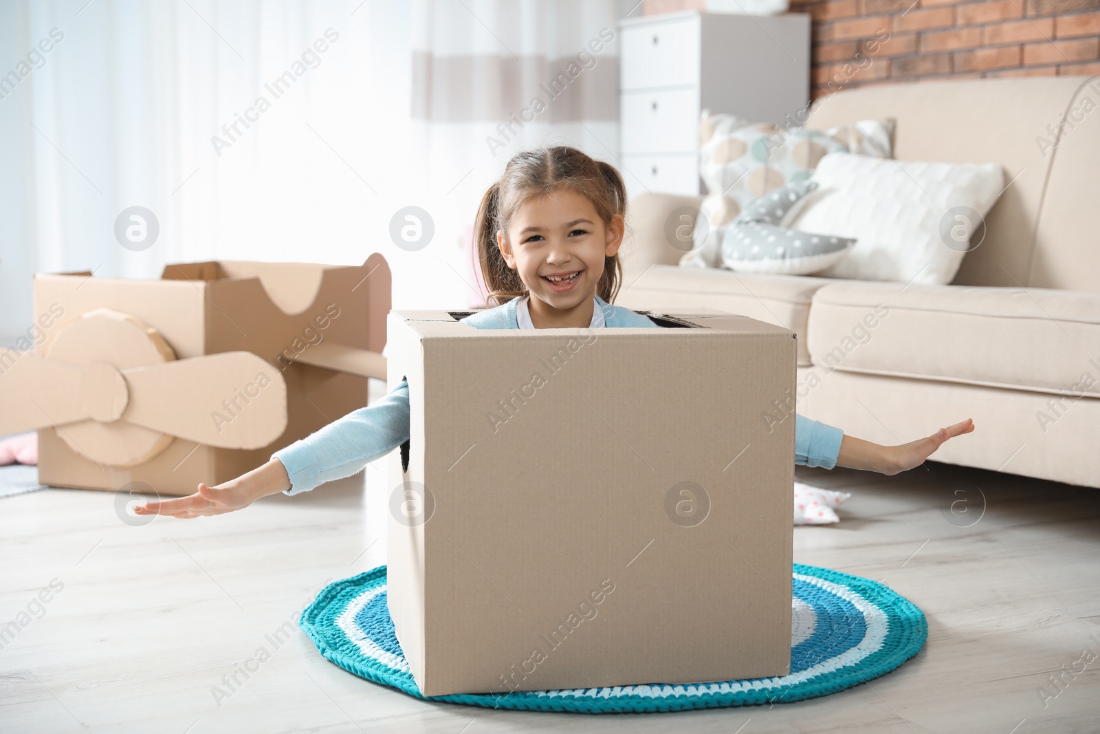 Photo of Cute little girl playing with cardboard box in living room