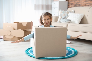 Cute little girl playing with cardboard box in living room