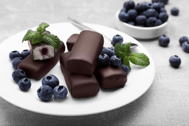 Photo of Delicious glazed curd snacks with fresh blueberries and mint on light grey table, closeup