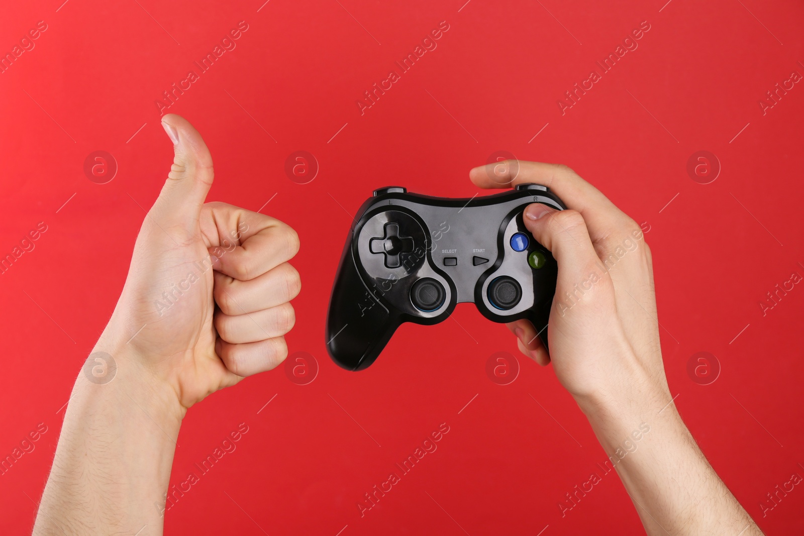 Photo of Man using wireless game controller and showing thumbs up on red background, closeup