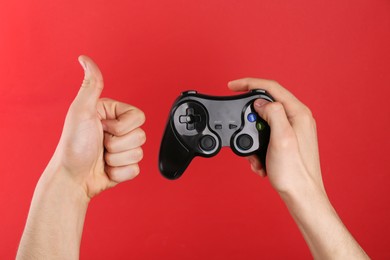 Man using wireless game controller and showing thumbs up on red background, closeup