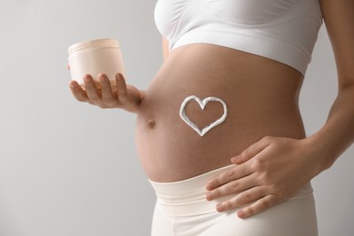 Young pregnant woman with cosmetic product on grey background, closeup