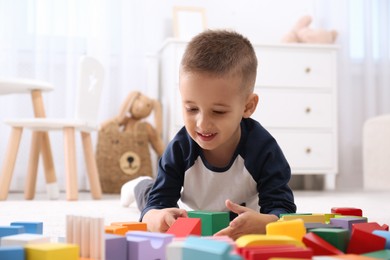 Photo of Cute little boy playing with colorful building blocks on floor in room