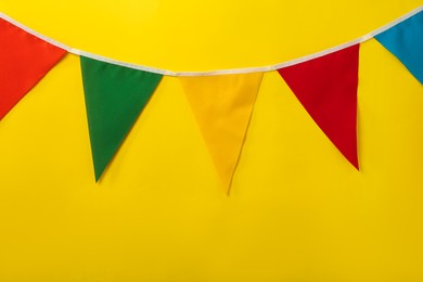 Photo of Bunting with colorful triangular flags on yellow background. Space for text