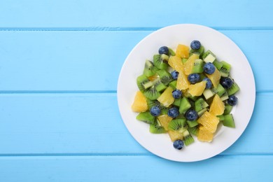 Photo of Plate of tasty fruit salad on light blue wooden table, top view. Space for text