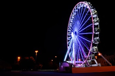 Photo of Beautiful glowing Ferris wheel on city street at night, space for text