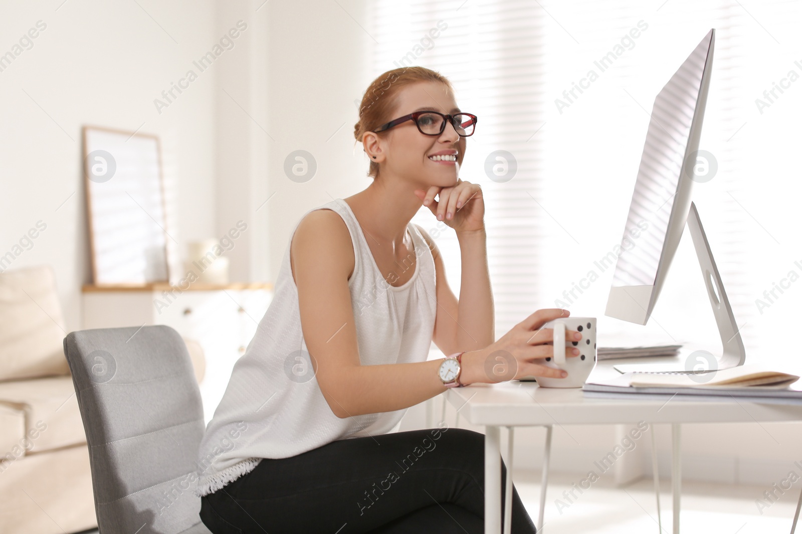 Photo of Young woman with cup of drink relaxing at table in office during break