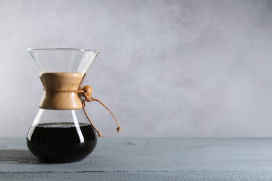 Photo of Glass chemex coffeemaker with drip coffee on grey wooden table. Space for text