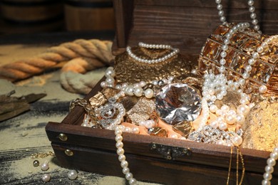 Photo of Chest with treasures and scattered sand on wooden floor, closeup