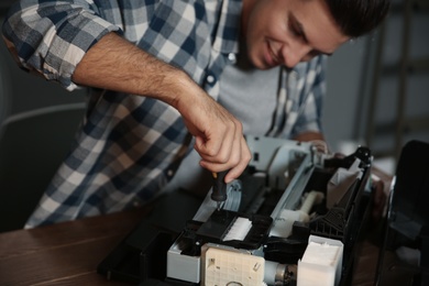 Repairman with screwdriver fixing modern printer indoors, closeup