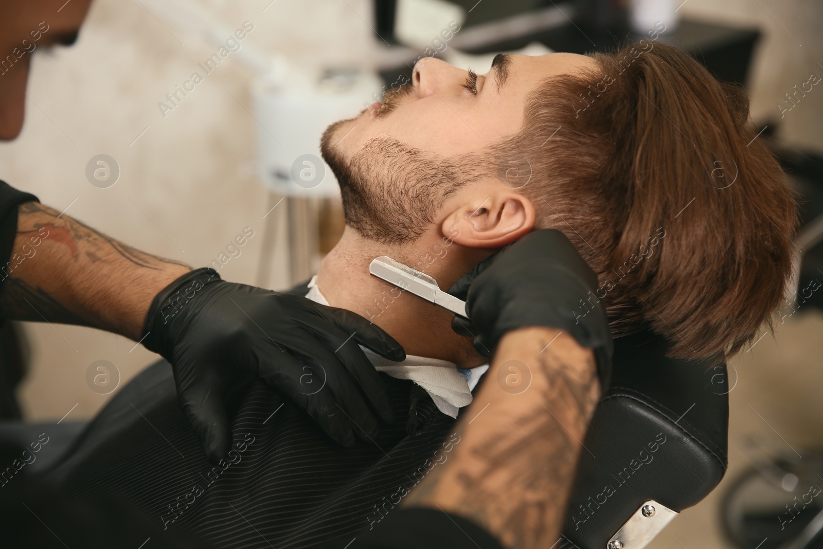 Photo of Professional hairdresser shaving client with straight razor in barbershop