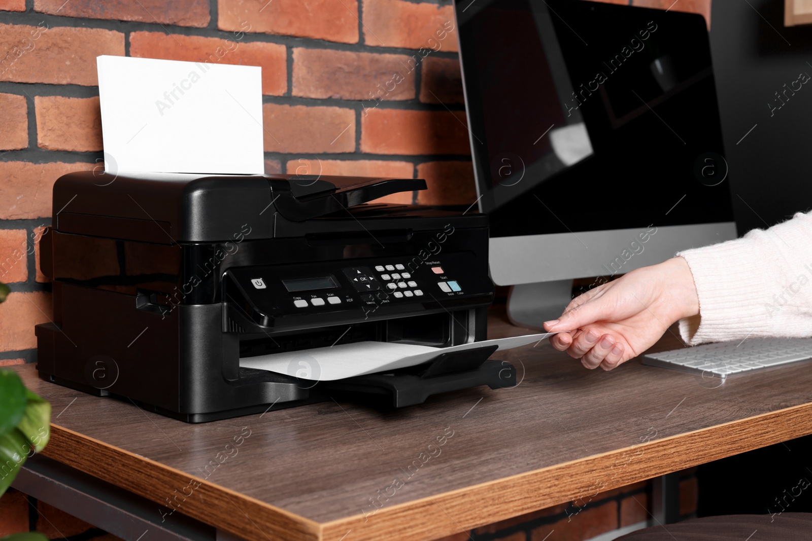 Photo of Woman using modern printer at wooden desk in home, closeup