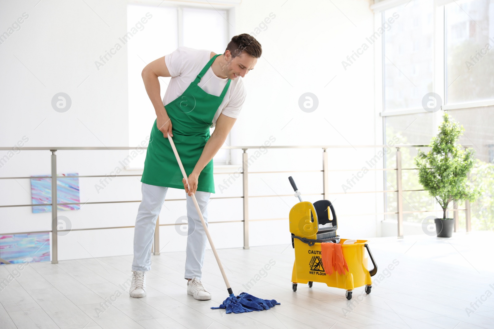 Photo of Young man with mop cleaning floor, indoors