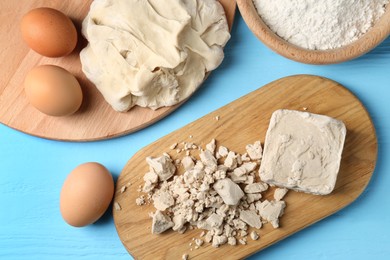 Photo of Pieces of compressed yeast, eggs, dough and flour on light blue wooden table, flat lay