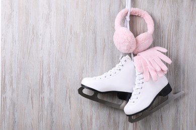 Pair of ice skates, warm earmuffs and gloves hanging on wooden wall, space for text