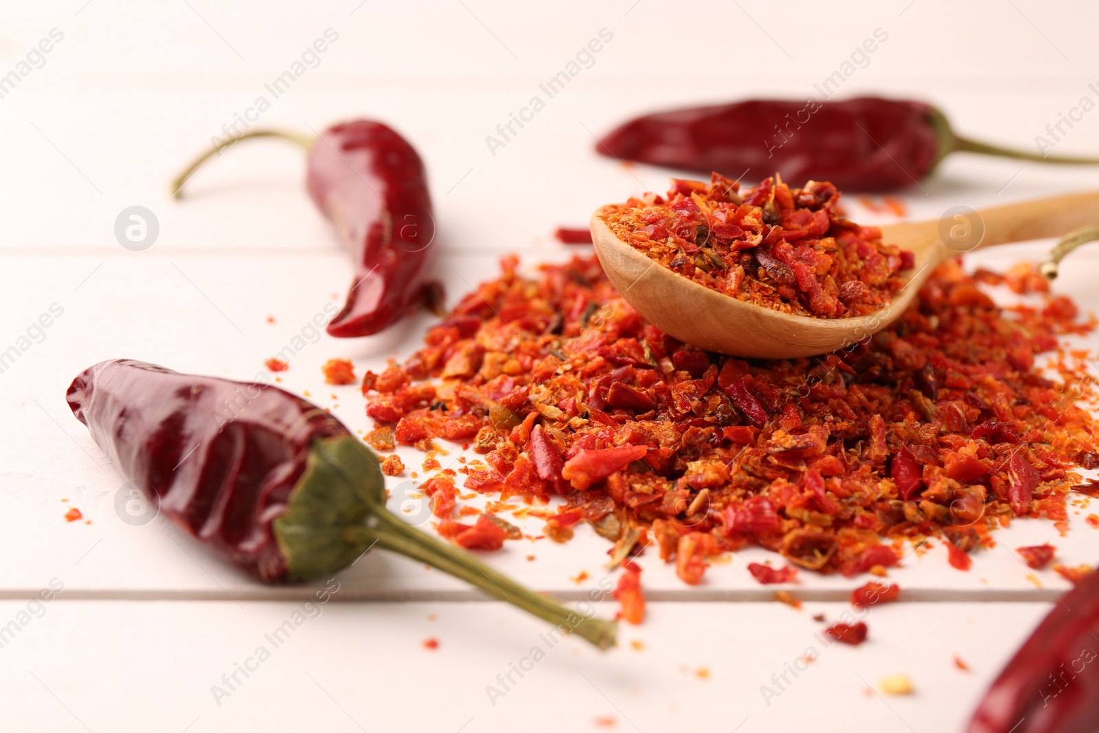 Photo of Chili pepper flakes and pods on white wooden table, closeup