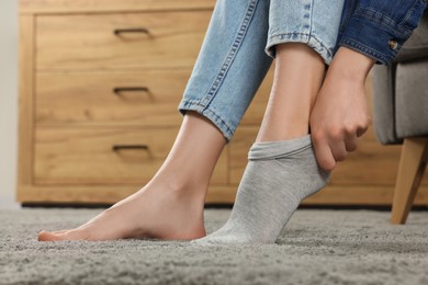 Photo of Woman putting on grey socks at home, closeup