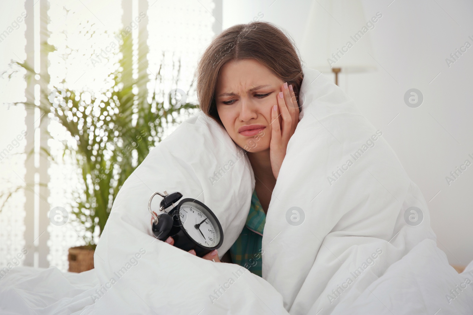 Photo of Sleepy young woman with alarm clock at home in morning