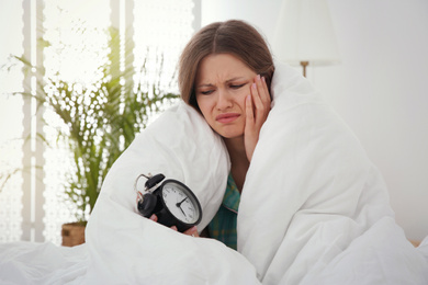 Photo of Sleepy young woman with alarm clock at home in morning