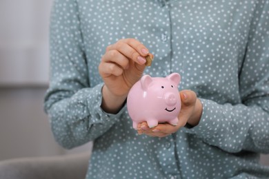 Young woman putting coin into piggy bank indoors, closeup