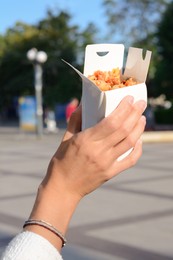 Woman holding paper box of takeaway noodles outdoors, closeup. Street food