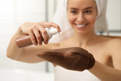 Photo of Self-tanning. Woman applying cosmetic product onto tanning mitt indoors, selective focus