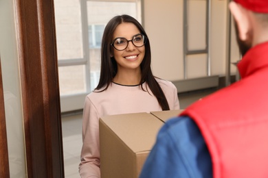 Photo of Woman receiving parcel from delivery service courier indoors