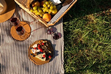 Red wine and different products for summer picnic served on blanket outdoors, flat lay