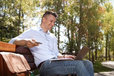 Photo of Man with smartphone working on laptop in park