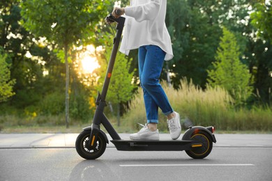 Woman riding modern electric kick scooter in park, closeup