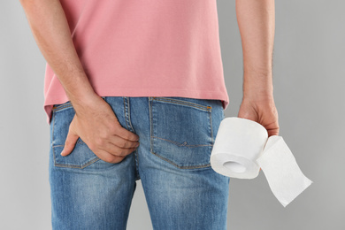 Man with toilet paper suffering from hemorrhoid on light grey background, closeup