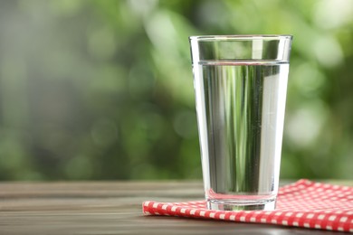 Photo of Glass of fresh water on wooden table outdoors. Space for text