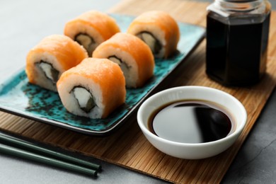 Photo of Tasty soy sauce and sushi rolls with salmon on grey table