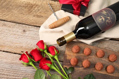Photo of Bottlered wine, chocolate truffles, corkscrew, gift box and roses on wooden table, above view