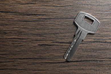 One key on wooden table, top view. Space for text