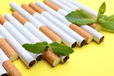 Photo of Menthol cigarettes and mint on yellow background, closeup