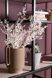 Photo of Stylish ceramic vase with dry plants on shelf near brown wall
