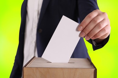 Woman putting her vote into ballot box on color background, closeup