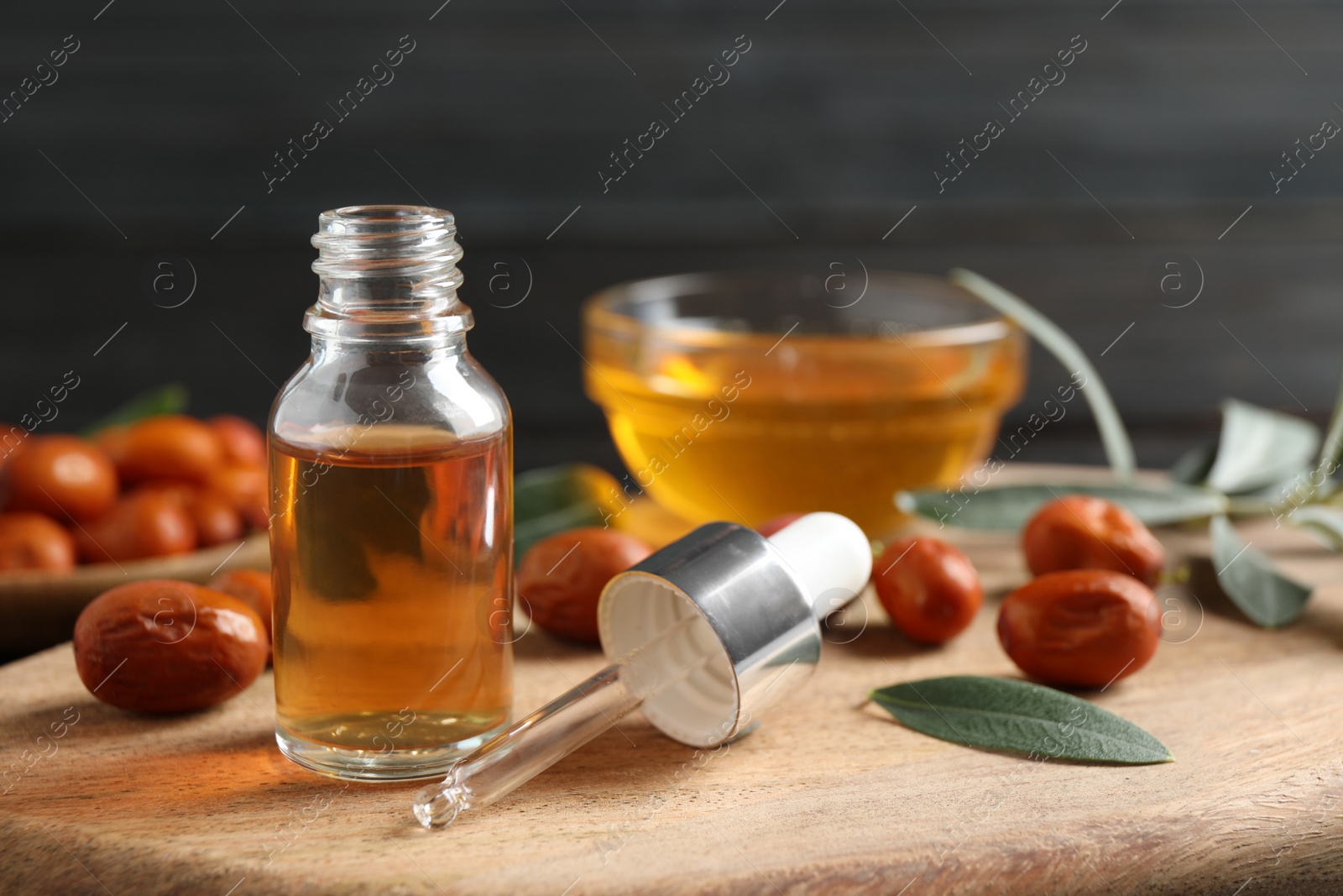 Photo of Glass bottle with jojoba oil and seeds on wooden board