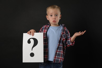 Photo of Confused boy holding sheet of paper with question mark on black background