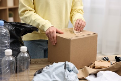 Photo of Woman with cardboard box separating garbage in room, closeup