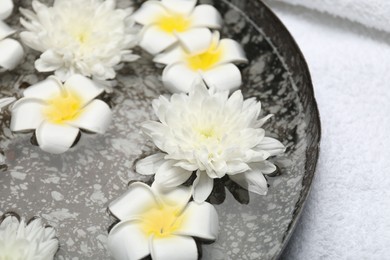 Photo of Bowl of water with flowers and towel on table, closeup. Spa treatment