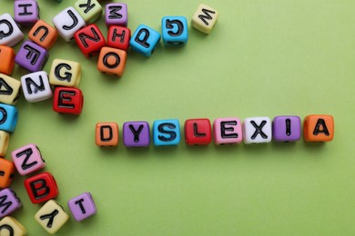 Photo of Colorful beads with word Dyslexia on light green background, flat lay